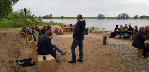 Menschen entspannen am Safari-Zelt am Flussufer, genießen die Natur und sitzen auf Holzbänken.
