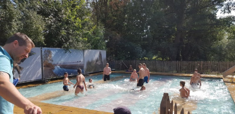 Folk leger i en udendørs pool ved Safari-teltet på Camping Elbeling i Tyskland, omgivet af træer.