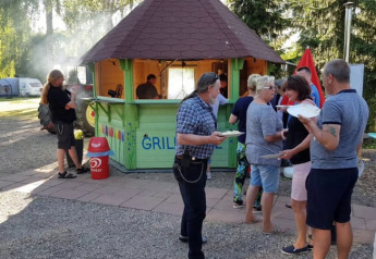 People gather around a grill hut at a campsite with tents and trees at Camping Elbeling, Germany.