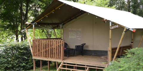 Safari tent at Camping L’Etruyère in France, elevated wooden deck with chairs, surrounded by trees.