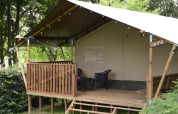 Tienda safari en Camping L’Etruyère en Francia con terraza de madera, entre vegetación y árboles.