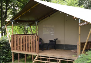 Tienda safari en Camping L’Etruyère en Francia con terraza de madera, entre vegetación y árboles.