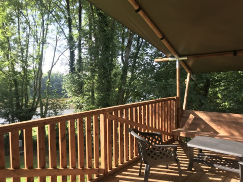 Blick von der Holzterrasse des Safari-Zeltes auf Camping L’Etruyère in Frankreich, umgeben von Bäumen.