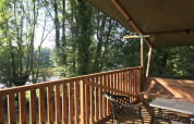 Blick von der Holzterrasse des Safari-Zeltes auf Camping L’Etruyère in Frankreich, umgeben von Bäumen.