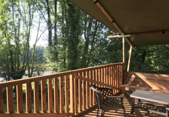 Blick von der Holzterrasse des Safari-Zeltes auf Camping L’Etruyère in Frankreich, umgeben von Bäumen.