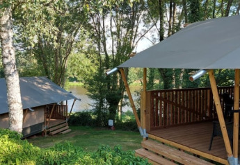 Safari tents at Camping L’Etruyère in France, surrounded by trees, wooden decks, and a nearby peaceful lake.