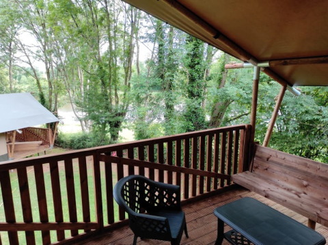 Blick von der Safari-Zeltterrasse auf Camping L’Etruyère in Frankreich mit Bäumen und Gartenmöbeln.