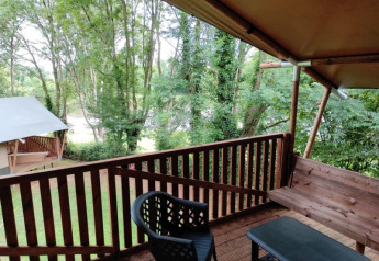 Vista desde una terraza de tienda safari en Camping L’Etruyère, Francia, con árboles y muebles exteriores.