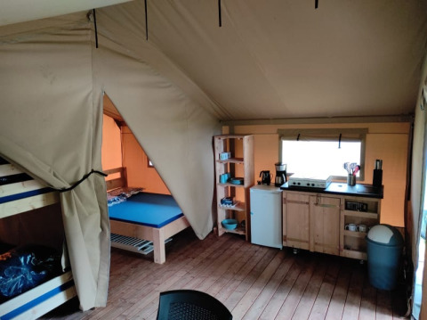 Innenansicht eines Safarizelts auf dem Campingplatz L’Etruyère in Frankreich mit Küche und Betten.