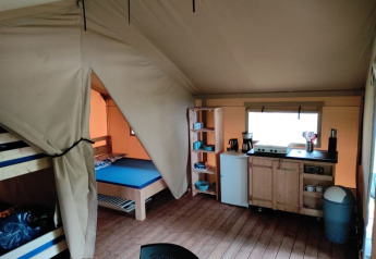 Vista interna di una tenda safari al Camping L’Etruyère in Francia, con cucina e zona notte.