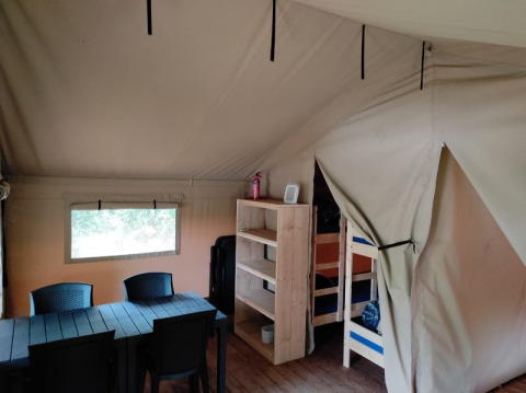 Interior of the safari tent at Camping L’Etruyère in France with table, chairs, shelves and bunk beds.