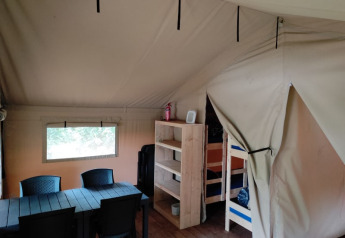 Interior of the safari tent at Camping L’Etruyère in France with table, chairs, shelves and bunk beds.