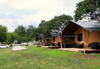 Safari telte på Camping Prima i Tjekkiet, med verandaer, grøn plæne og nogle træer foran teltene.