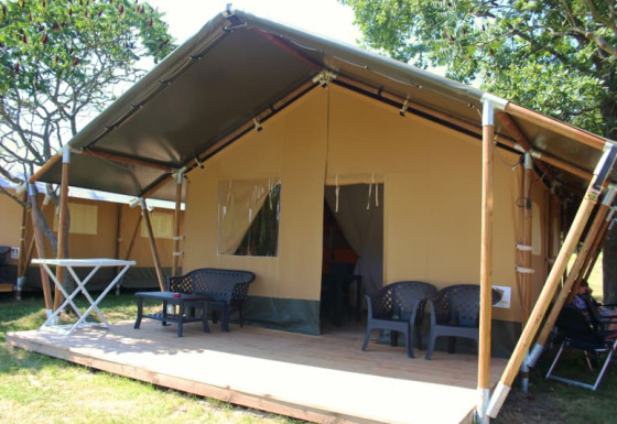 Safari tent with a covered wooden terrace, outdoor seating, and greenery in a relaxing camping area.