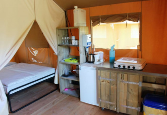 Safari tent at Camping Prima in Czech Republic with bed, kitchenette, and rustic wooden cabinets inside.