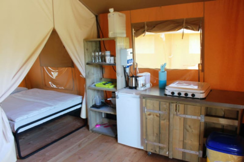 Safari tent at Camping Prima in Czech Republic with bed, kitchenette, and rustic wooden cabinets inside.