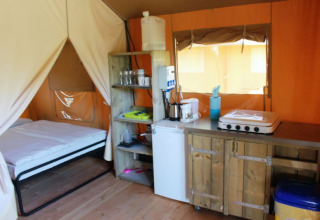 Tienda safari en Camping Prima, República Checa, con cama, cocina y muebles rústicos de madera.