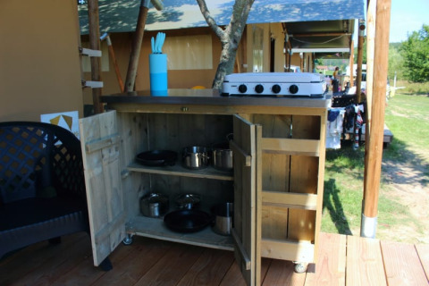 Cucina esterna accanto a tenda safari al Camping Prima in Repubblica Ceca con fornello, pentole e utensili.