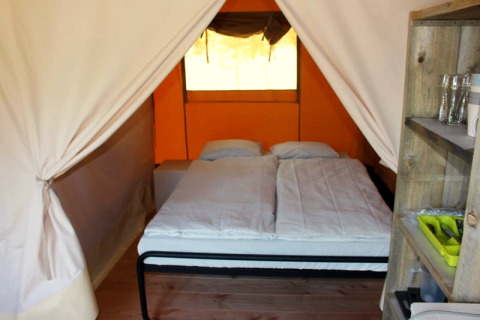 Binnenaanzicht van een safaritent op Camping Prima in Tsjechië, met tweepersoonsbed en rekken.
