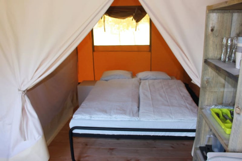 Vista interior de una tienda safari en Camping Prima en República Checa, con cama doble y estantería.