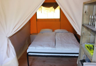Vista interior de una tienda safari en Camping Prima en República Checa, con cama doble y estantería.