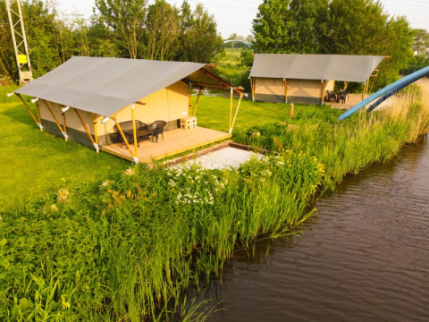Safaritenten aan het water bij Camping Pasveer in Nederland, omgeven door gras en een rustige natuur.