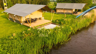 Safarizelte auf Camping Pasveer in den Niederlanden, mit Blick auf einen kleinen Fluss und grüne Wiese.