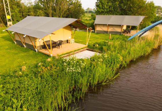 Safarizelte auf Camping Pasveer in den Niederlanden, mit Blick auf einen kleinen Fluss und grüne Wiese.