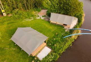 Vista aérea de tiendas safari en Camping Pasveer, Países Bajos, junto a un río y rodeadas de vegetación.