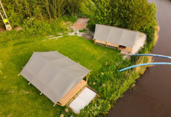 Luftaufnahme von Safari-Zelten auf Camping Pasveer in den Niederlanden, neben einem Fluss gelegen.