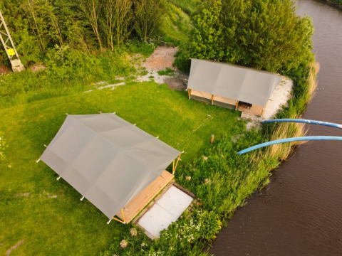 Luftaufnahme von Safari-Zelten auf Camping Pasveer in den Niederlanden, neben einem Fluss gelegen.