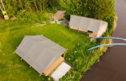 Aerial view of safari tents at Camping Pasveer in the Netherlands, set by a river and lush greenery.