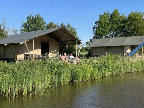 Safaritent aan het water bij Camping Pasveer in Nederland, omringd door groen gras en blauwe lucht.