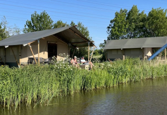 Safari-Zelt auf dem Campingplatz Pasveer in den Niederlanden, am Wasser mit üppigem grünen Gras.