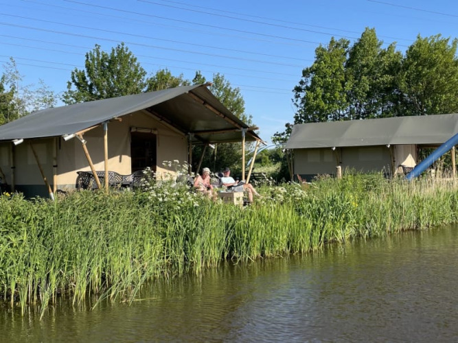 Tienda safari en Camping Pasveer, Países Bajos, junto a un canal y rodeada de vegetación verde.