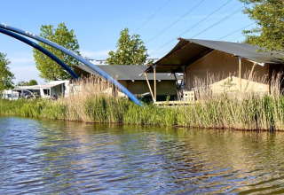 Safari telt ved Camping Pasveer i Holland med udsigt til vand, siv og blå buer i baggrunden.