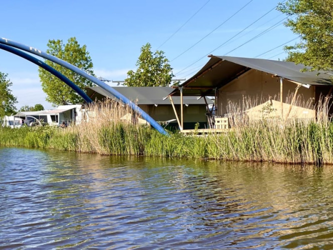 Tienda safari en Camping Pasveer, Países Bajos, junto al agua, cañas y grandes arcos azules.