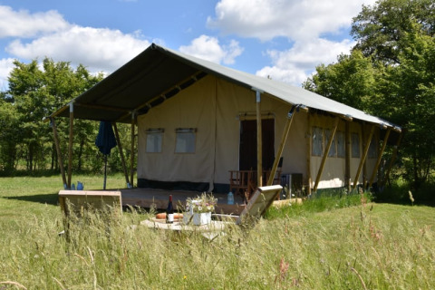 Tenda safari al Camping Domaine Bleu Celeste in Francia, immersa nel verde con alberi e cielo sereno.