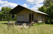 Tienda safari en Camping Domaine Bleu Celeste en Francia, rodeada de césped y árboles bajo un cielo azul.