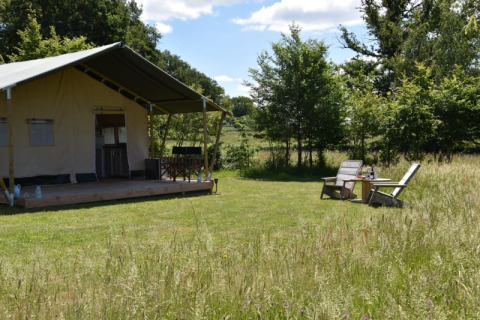Safari-Zelt auf dem Campingplatz Domaine Bleu Celeste in Frankreich mit Terrasse und zwei Stühlen im Grünen.