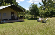 Tienda safari en Camping Domaine Bleu Celeste en Francia, con porche y dos sillas en un campo verde.