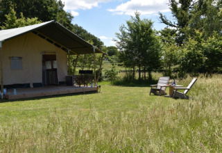 Tienda safari en Camping Domaine Bleu Celeste en Francia, con porche y dos sillas en un campo verde.
