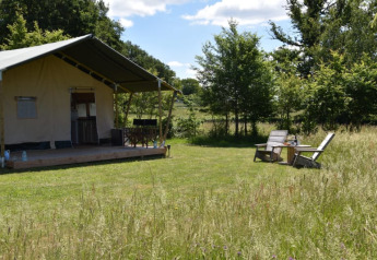 Safari tent at Camping Domaine Bleu Celeste in France with a porch and two chairs set on a grassy meadow.