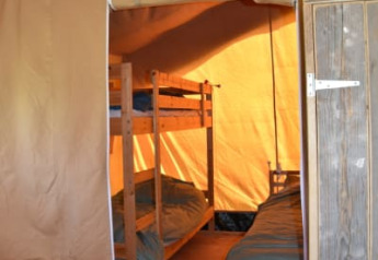 Indvendig udsigt af en safaritelt med køjesenge og trægulv på Camping Domaine Bleu Celeste i Frankrig.
