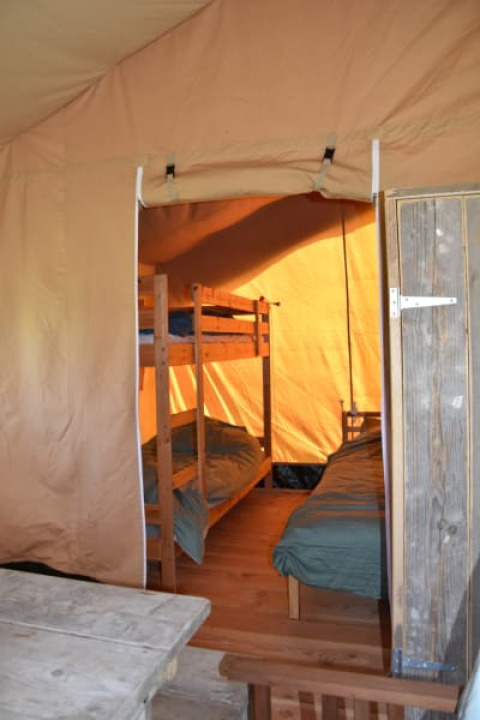 Indvendig udsigt af en safaritelt med køjesenge og trægulv på Camping Domaine Bleu Celeste i Frankrig.