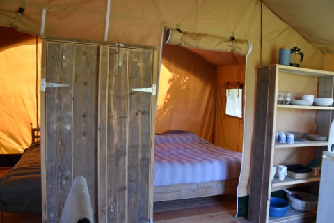 Interno di una tenda safari al Camping Domaine Bleu Celeste in Francia con letto e scaffali da cucina.