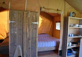 Interno di una tenda safari al Camping Domaine Bleu Celeste in Francia con letto e scaffali da cucina.