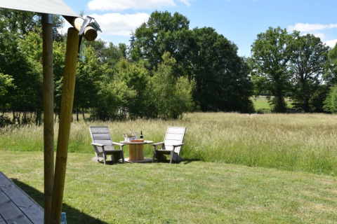 Zwei Holzstühle und ein Tisch auf einer Wiese vor einem Safarizelt mit Blick auf Felder und Bäume in Frankreich.