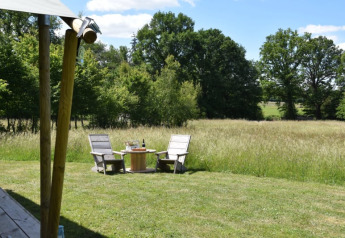 Two wooden chairs and a table on the grass in front of a safari tent overlooking fields and trees in France.