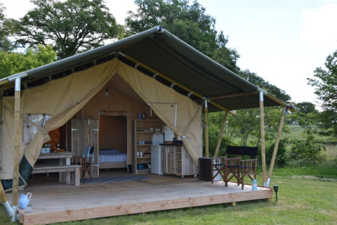 Safari tent at Camping Domaine Bleu Celeste in France, featuring a deck, rustic furniture and scenic nature.